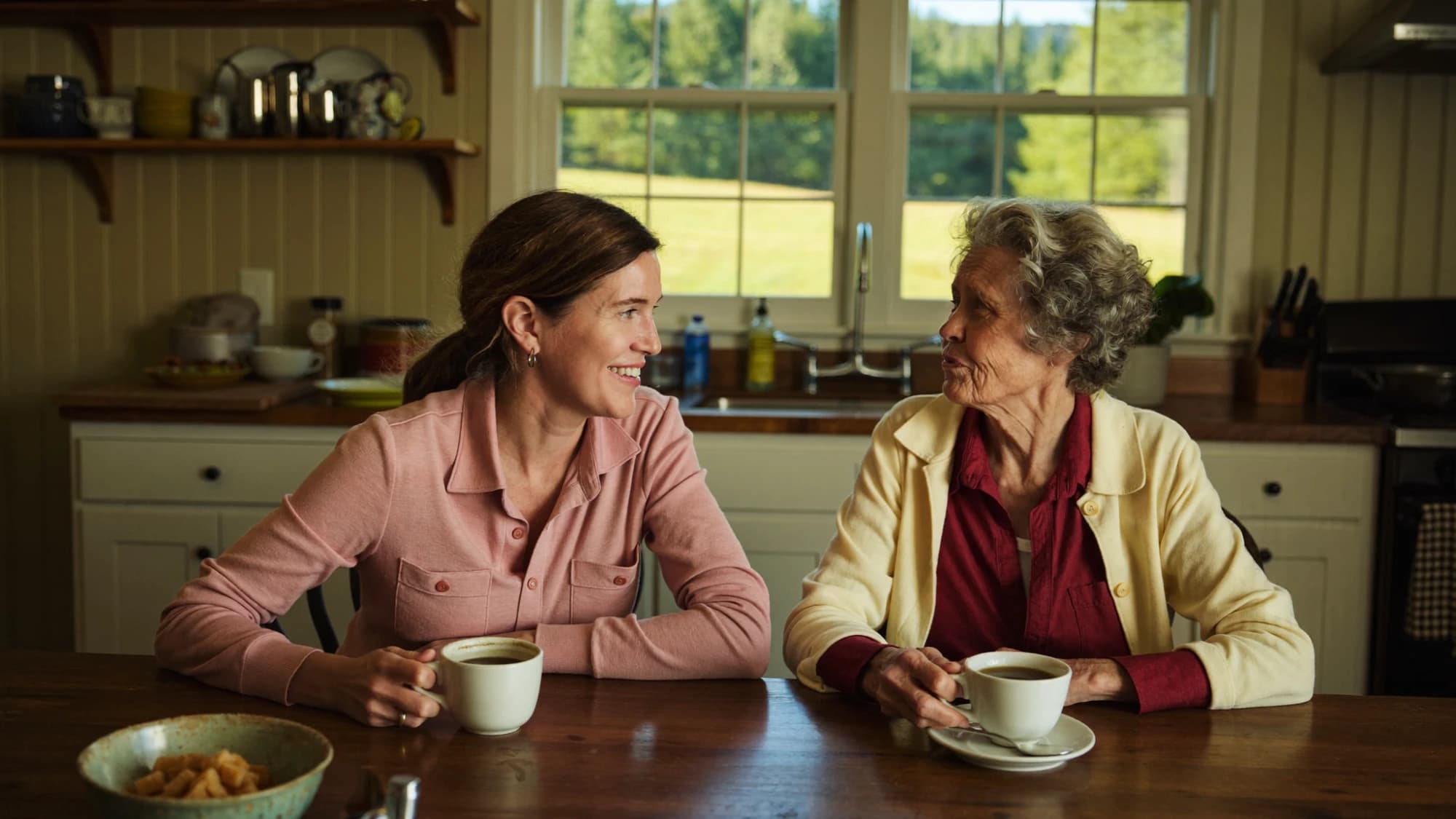 An adult daughter and her aging mother talking over coffee at a kitchen table