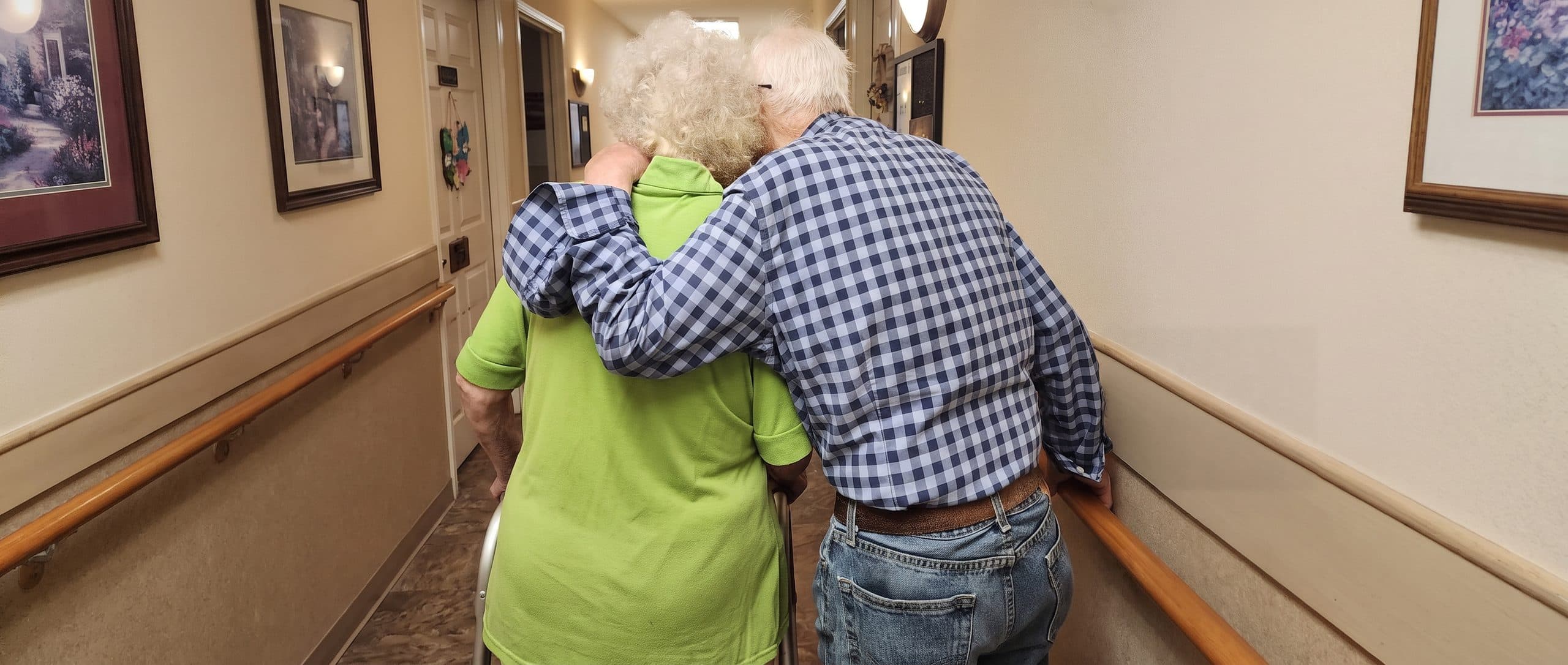 Two residents walking arm in arm down a hallway at an Aspen Leaf home