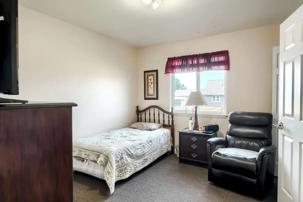 Private resident bedroom with bed, dresser, television, and recliner at Aspen Leaf Stratton