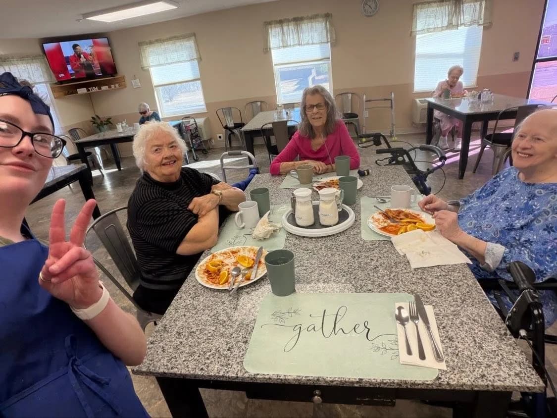 A caregiver and three residents smiling around the dining table after breakfast at an Aspen Leaf home