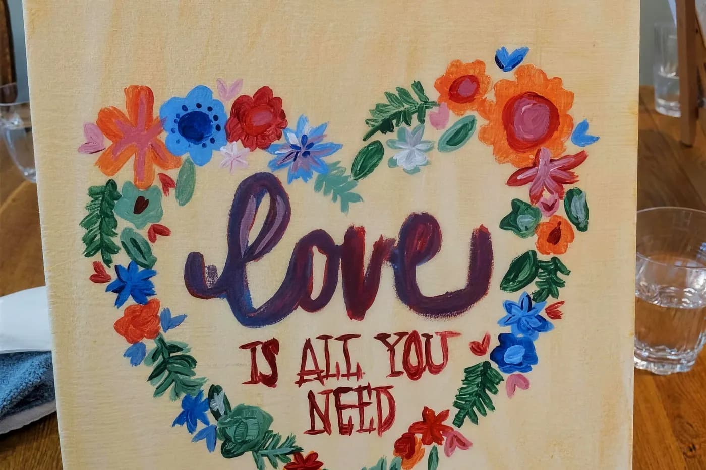 A resident's finished painting reading Love Is All You Need, on an easel at Aspen Leaf