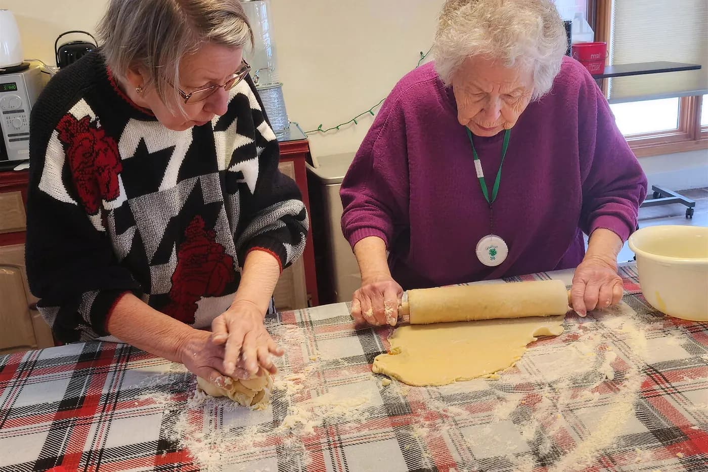 A resident and a caregiver rolling out dough together at an Aspen Leaf home